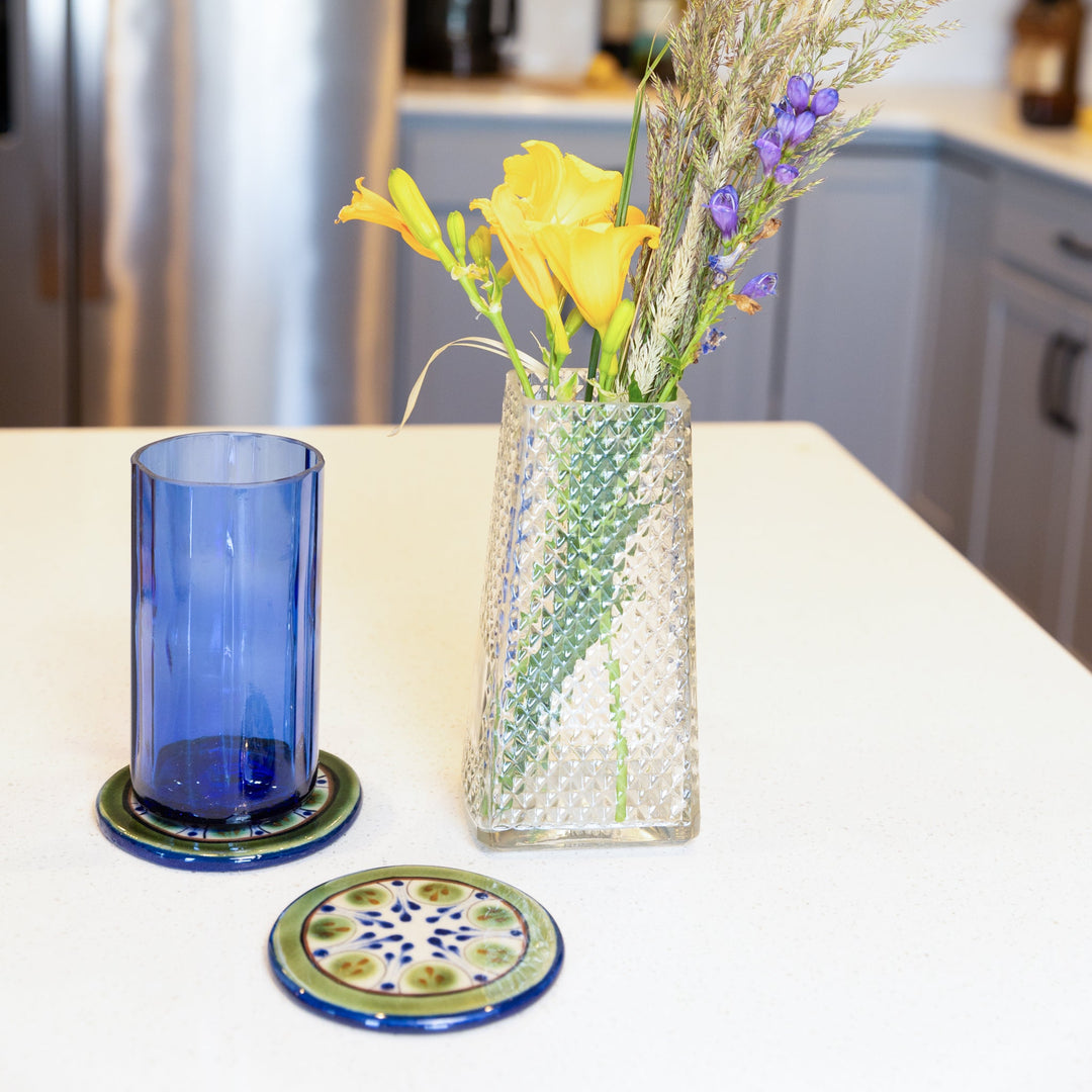 Round ceramic coaster with blue border and green floral motif.