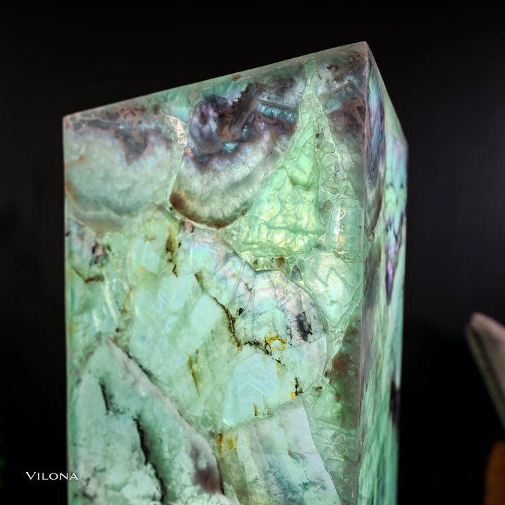 Close-up of glowing green fluorite square prism lamp with dark inclusions and purple tones