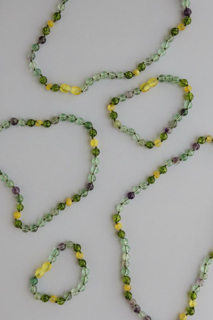 Gemstone bead necklaces in green, yellow, and purple on a neutral background