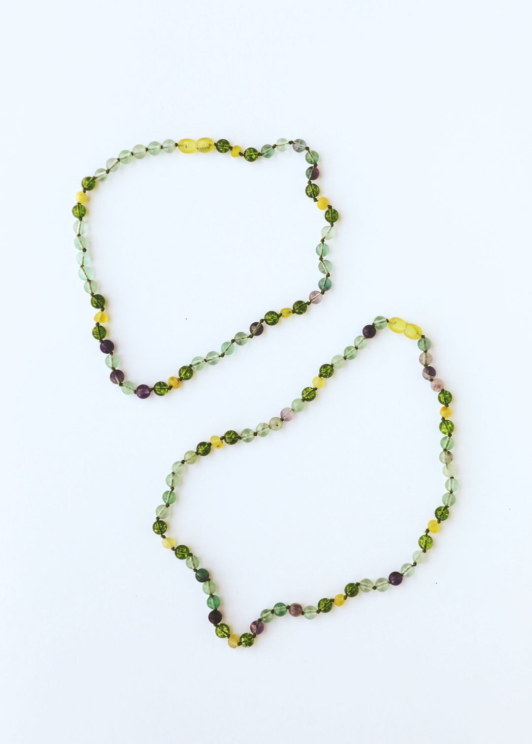 Two looping gemstone bead necklaces, green and yellow with small purple accents