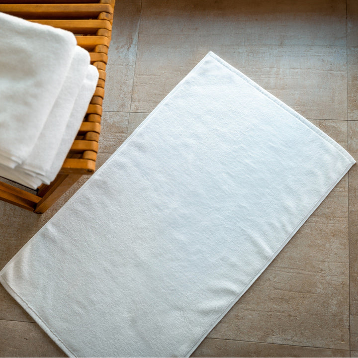 White bath mat with clean edges, shown flat on a tiled bathroom floor.