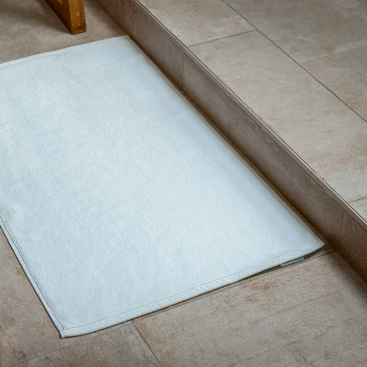 White bath mat with flat border edge on bathroom floor