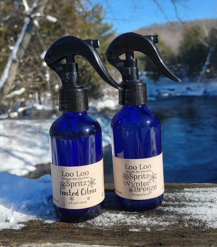 Two deodorizing spray bottles, blue glass with black triggers, Frosted Citrus and Winter Breeze