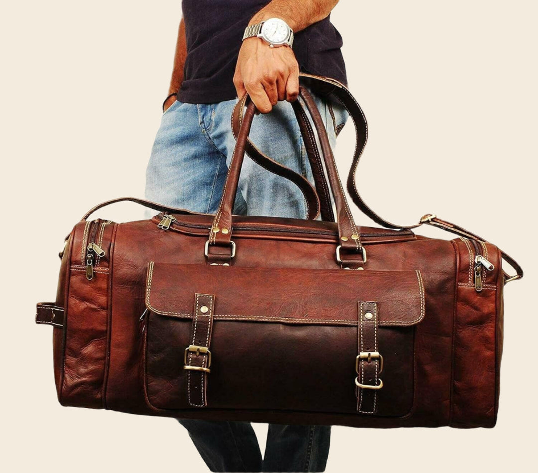 Brown leather duffel bag with front pocket and long shoulder strap, held by handle