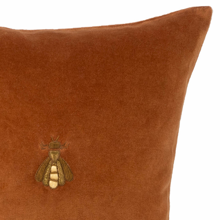 Brown velvet throw pillow corner with embroidered bee logo, tight close-up