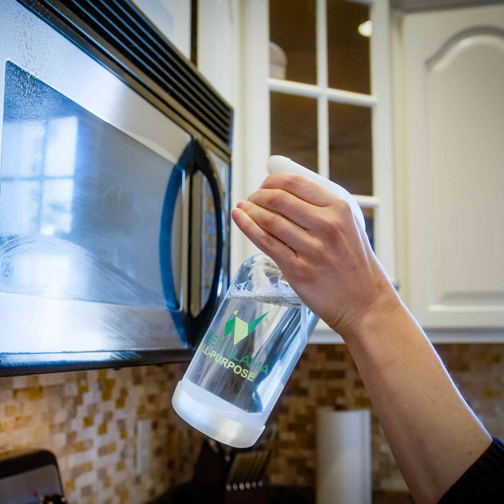 Hand holding a lemongrass cleaner refill bottle near a stovetop