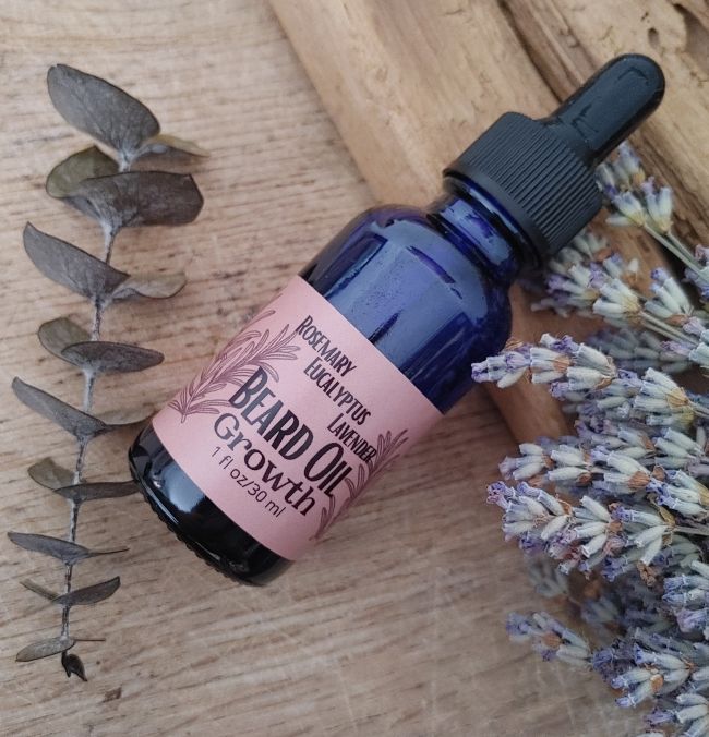 Blue glass beard oil bottle with black dropper and pink label reading &