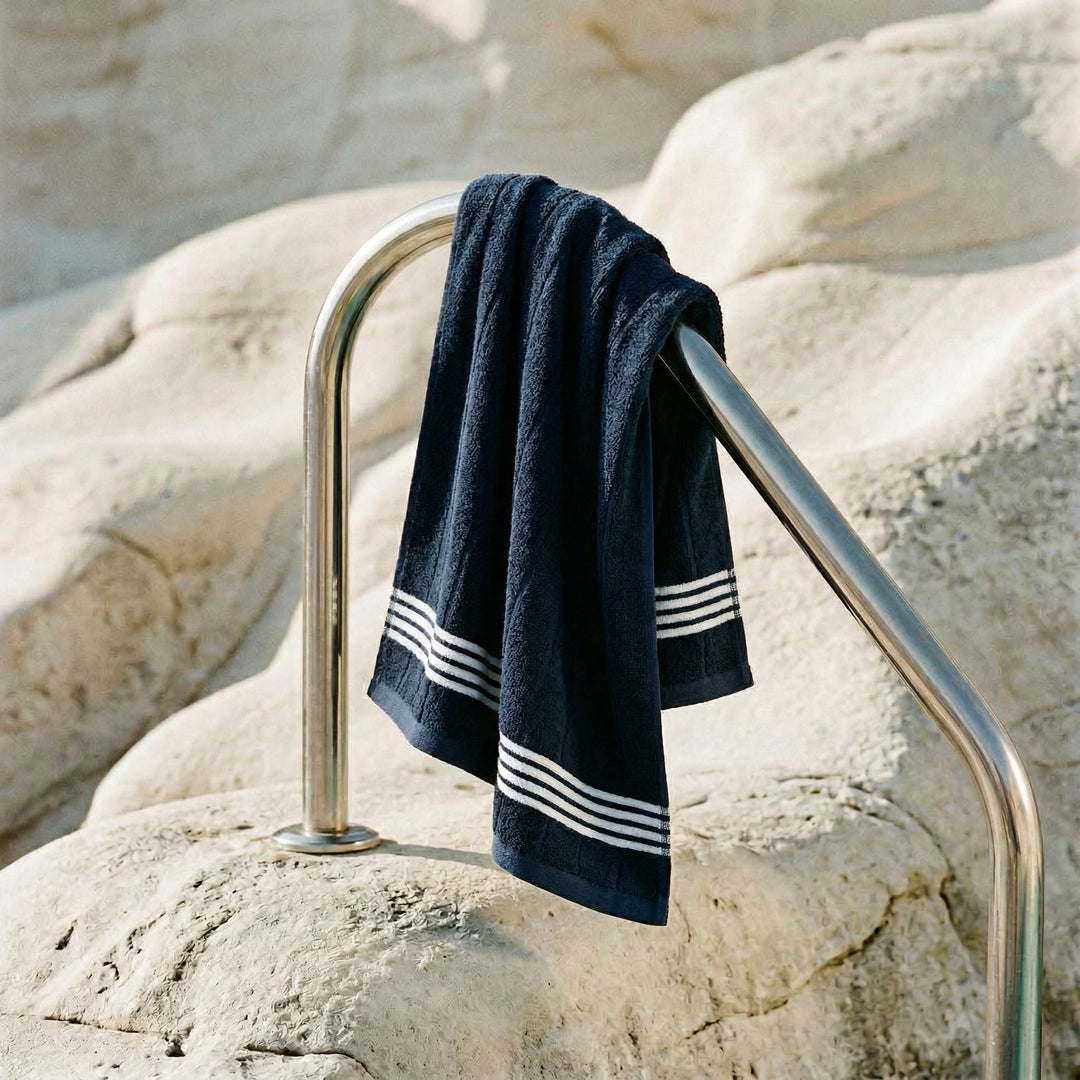 Dark navy cotton towel with white stripe bands, draped over metal rail