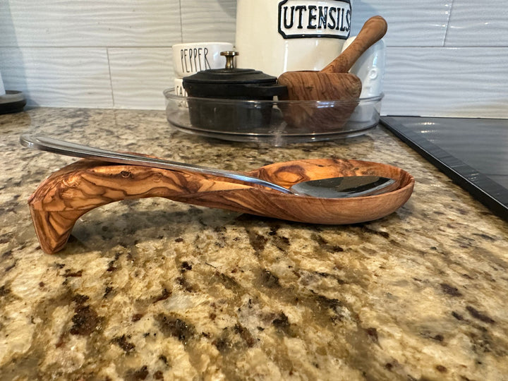 Olive wood spoon rest tray holding a wooden spoon on a countertop