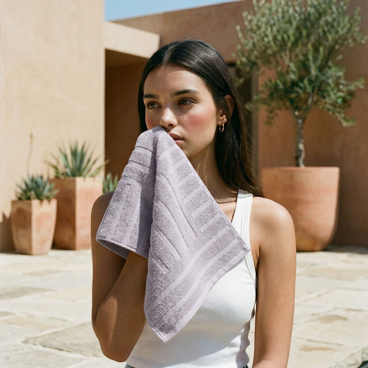Lilac cotton towel folded, held in front of a person wearing a white tank top.