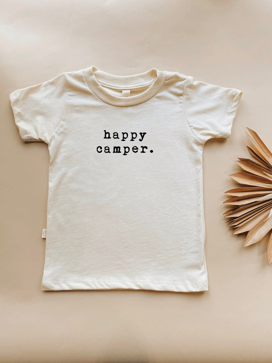 Toddler short-sleeve crewneck T-shirt in light cream with centered 'happy camper.' print