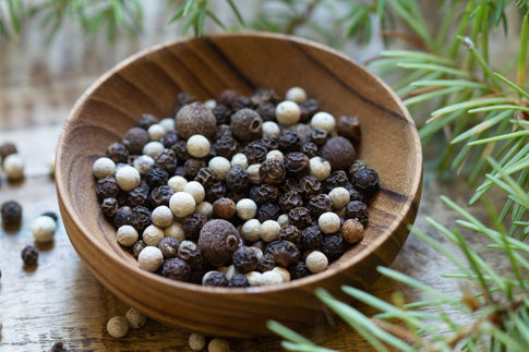 Peppercorn blend in wooden bowl with mixed black, white, and tan whole peppercorns