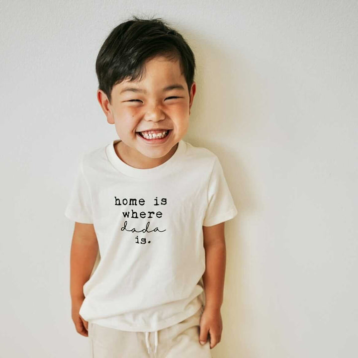 Kids organic T-shirt in cream on smiling child, 'home is where dada is' front print.