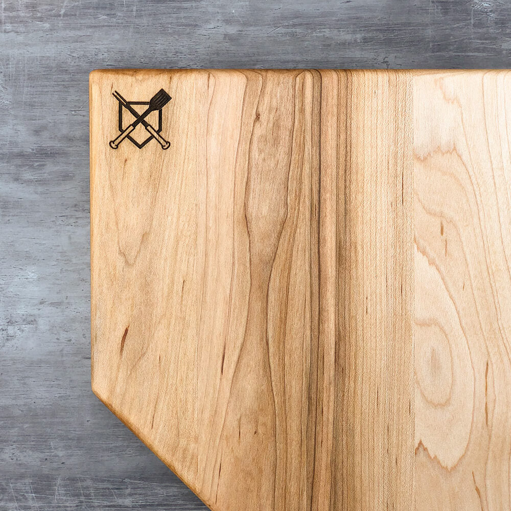 Home plate cutting board front view, light wood with dark center stripe, engraved crossed logo