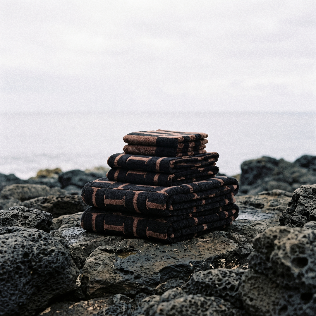 Stack of folded cotton towels on textured rocks, dark base with brown grid pattern