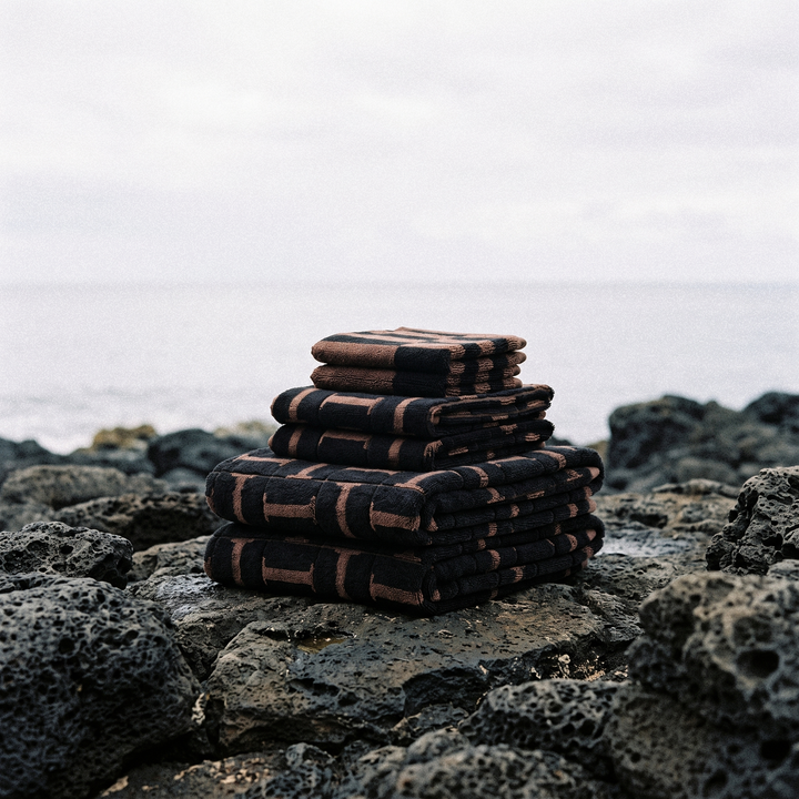 Stack of folded cotton towels on textured rocks, dark base with brown grid pattern