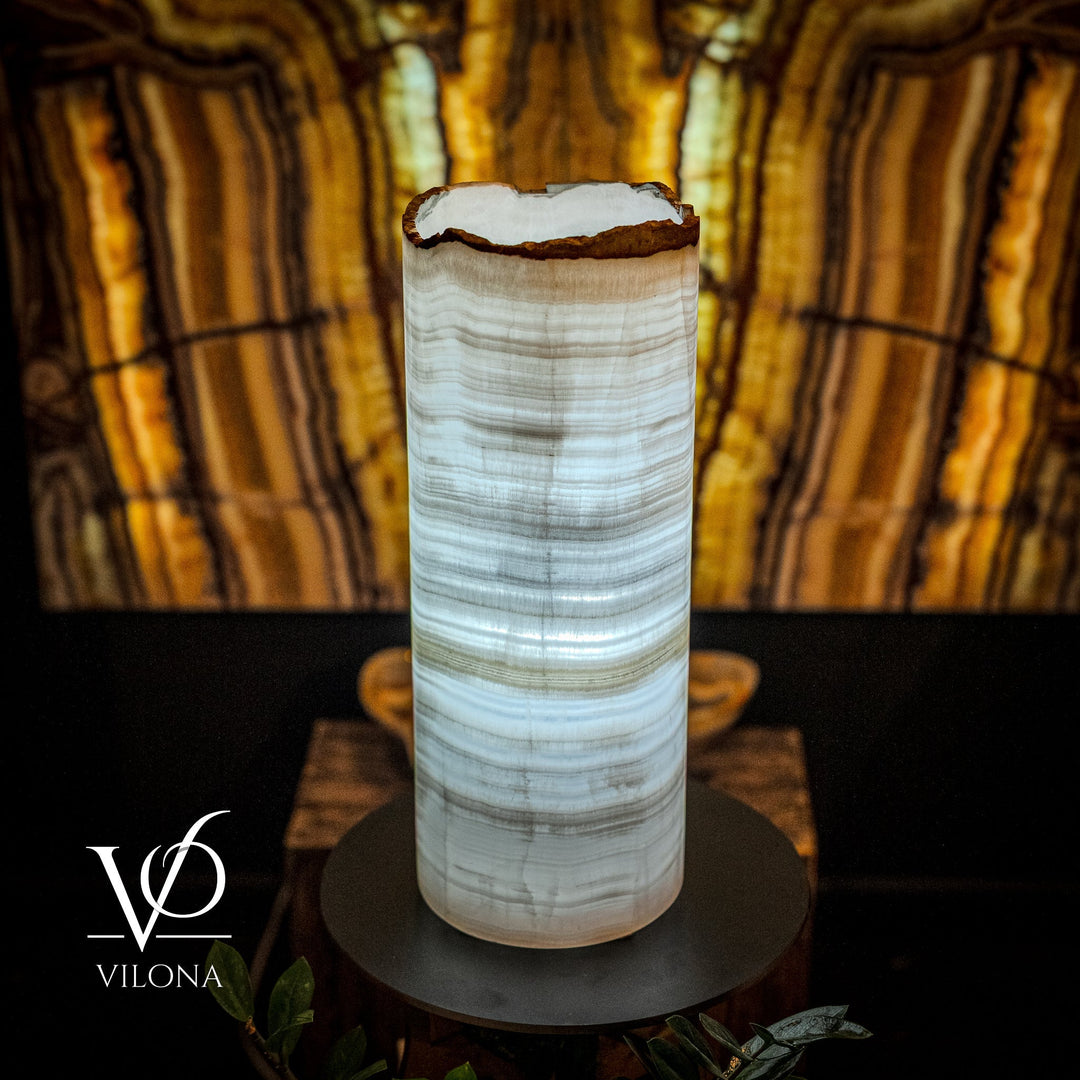 Table lamp with cylindrical onyx shade and round black base; white veining with blue tint