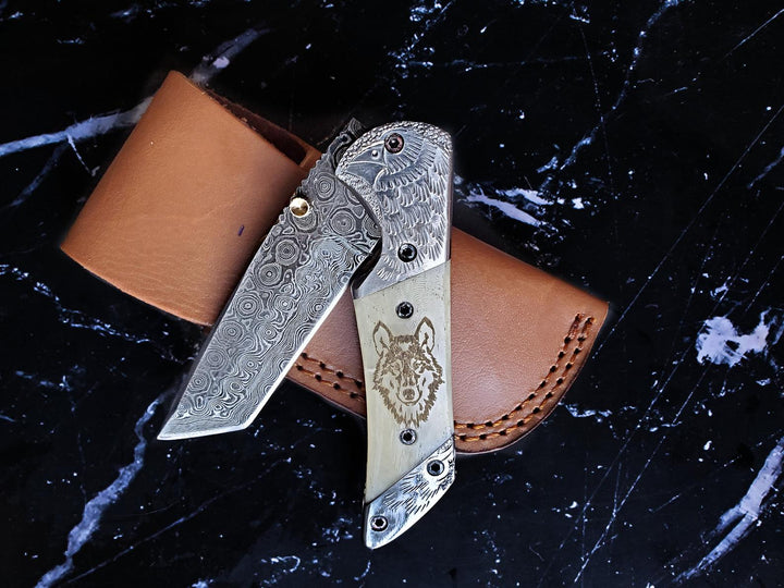 Engraved steel folding knife with damascus blade and tan leather sheath, eagle wolf etching