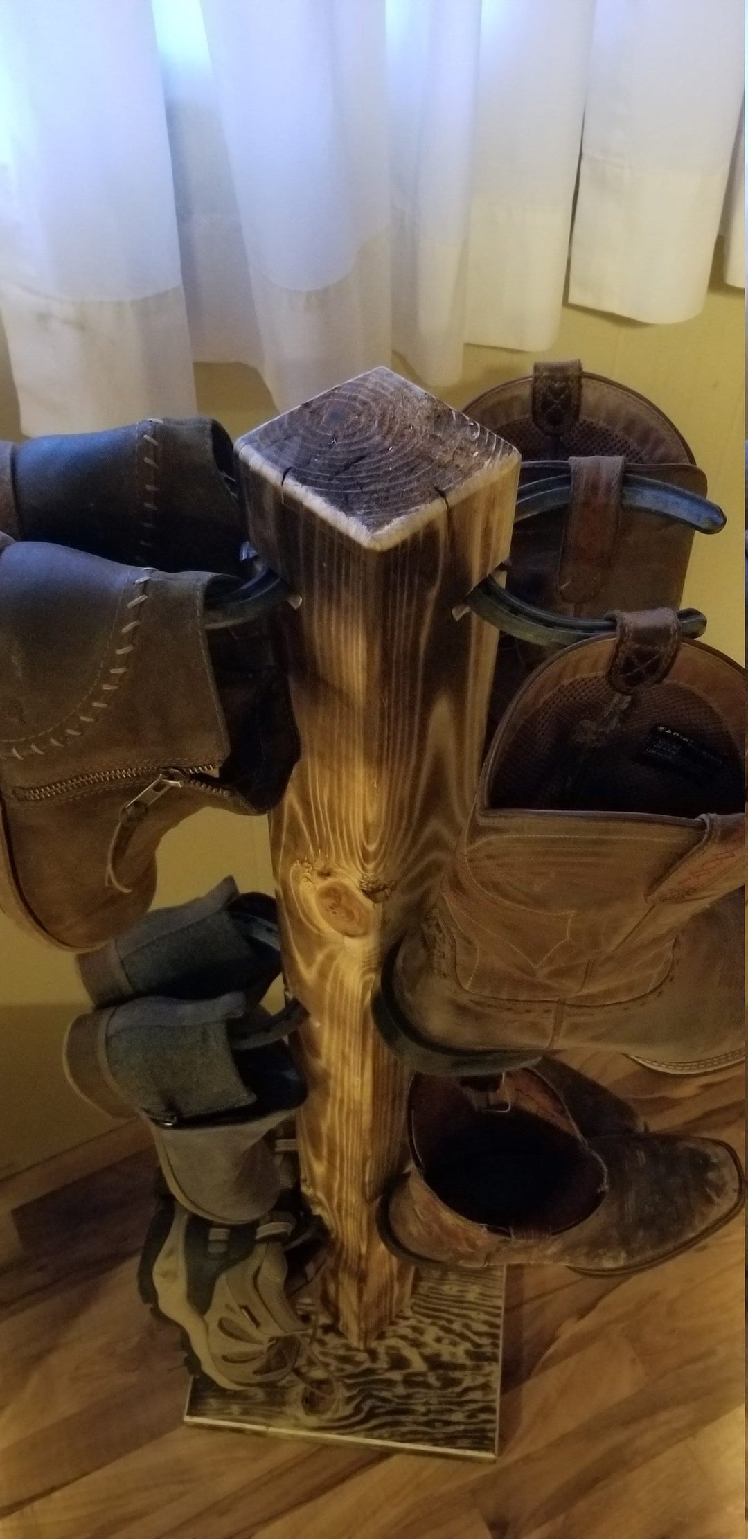 Wooden cowboy boot floor stand with square top and side pegs, holding boots.