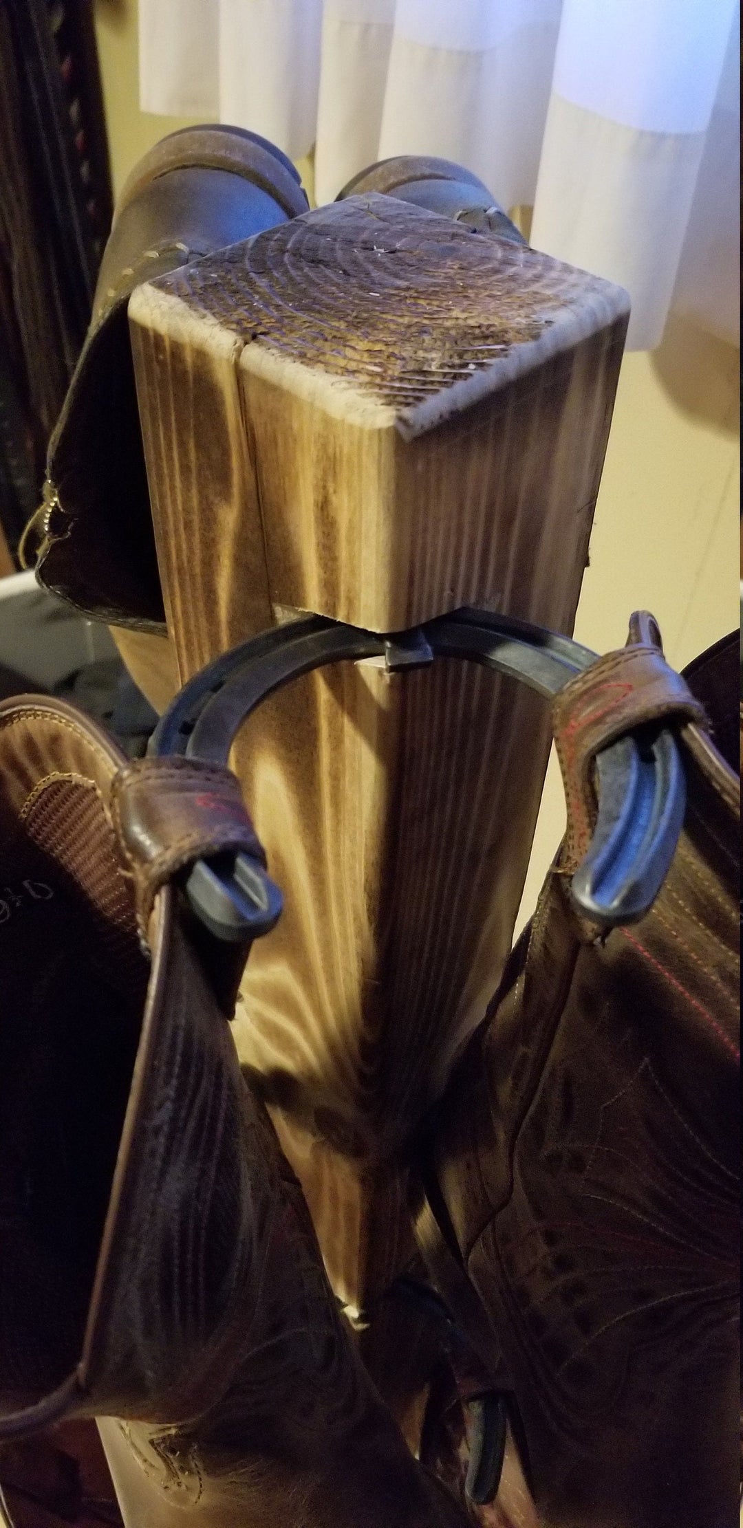 Close-up of wooden cowboy boot floor stand post with side pegs and boot straps.