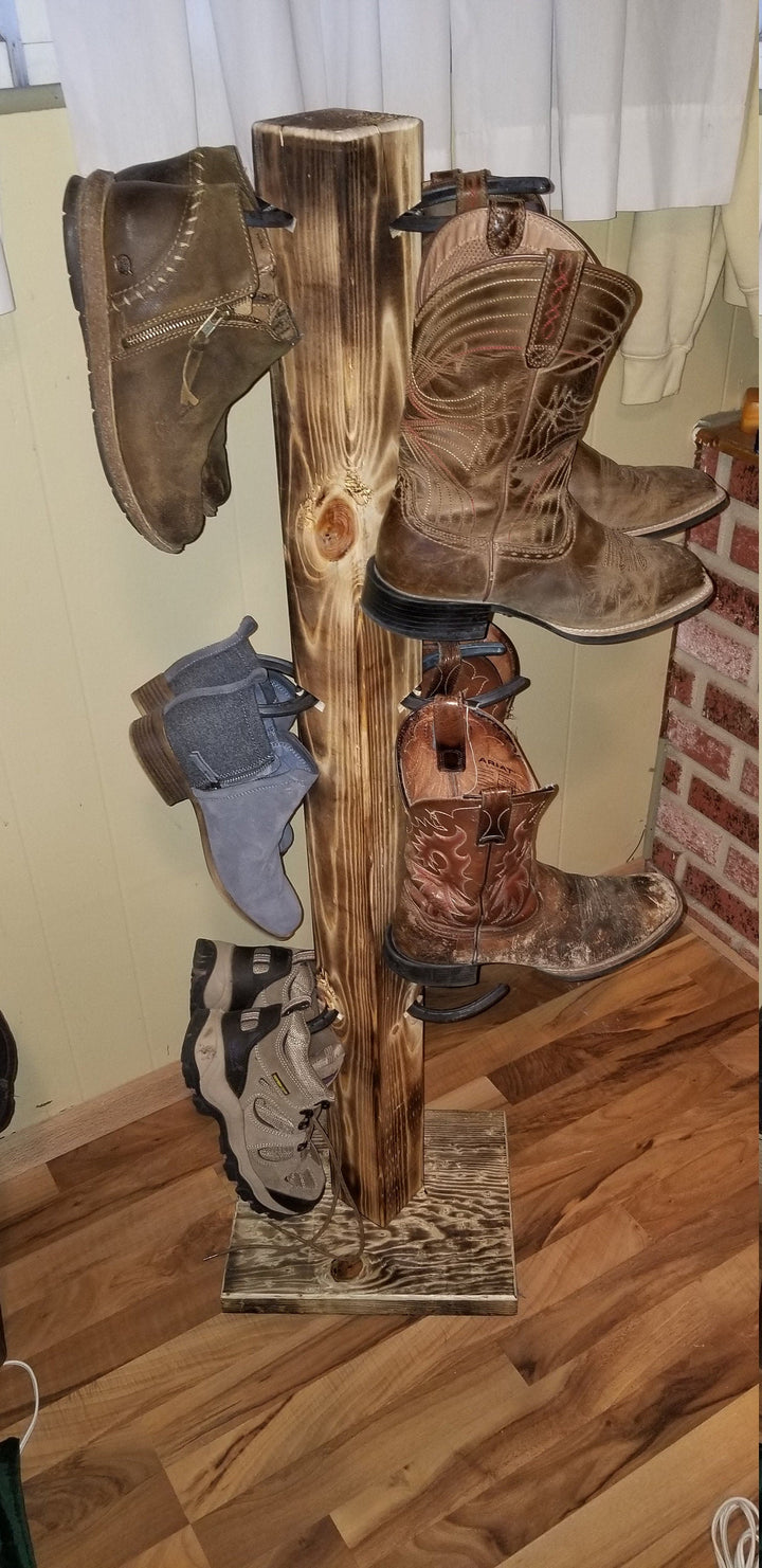 Carved wooden cowboy boot floor stand with pegs holding several cowboy boots.