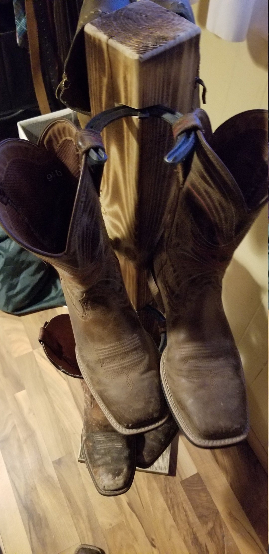 Angled view of wooden cowboy boot floor stand with boots mounted on side pegs.