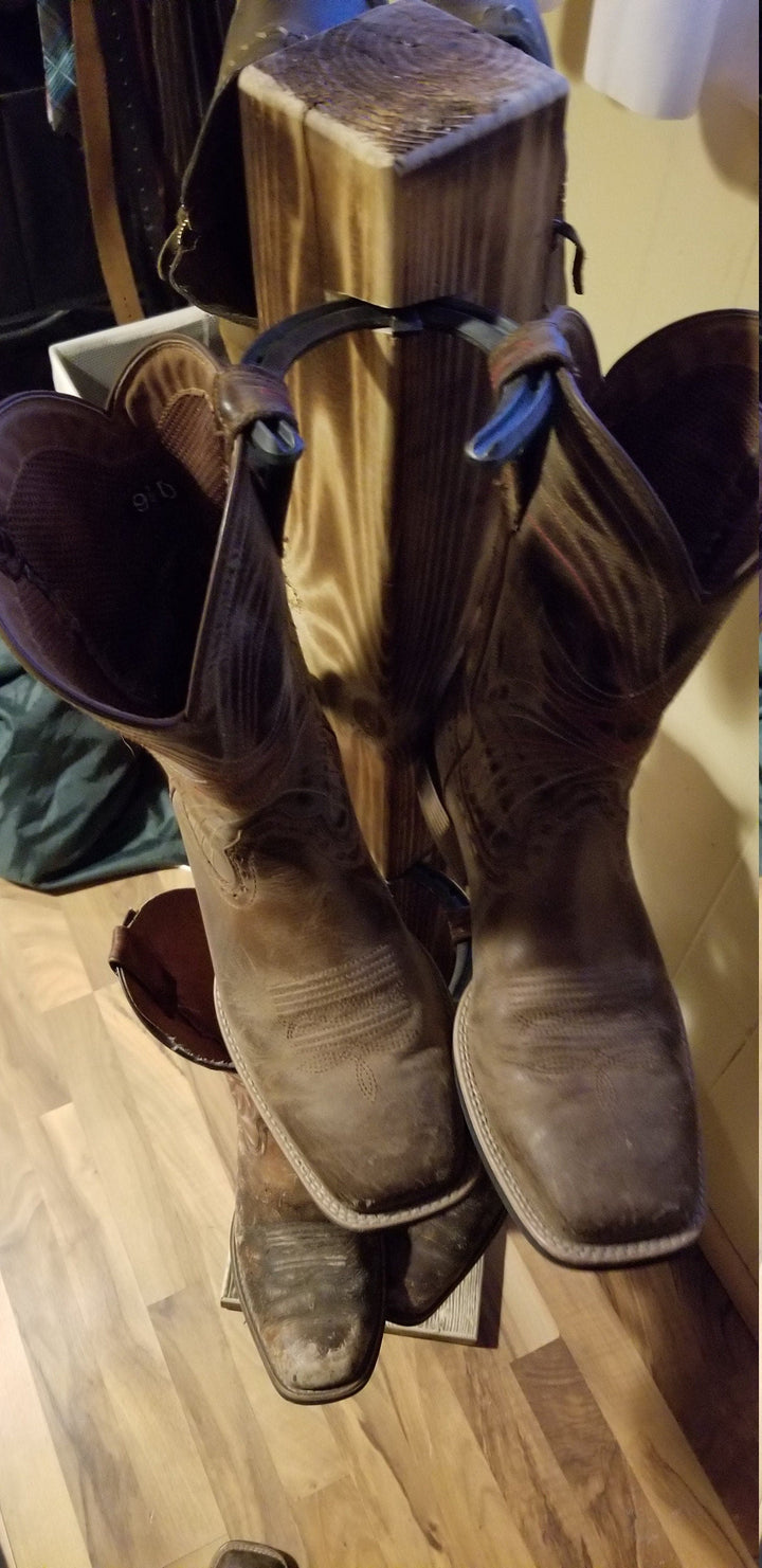 Angled view of wooden cowboy boot floor stand with boots mounted on side pegs.