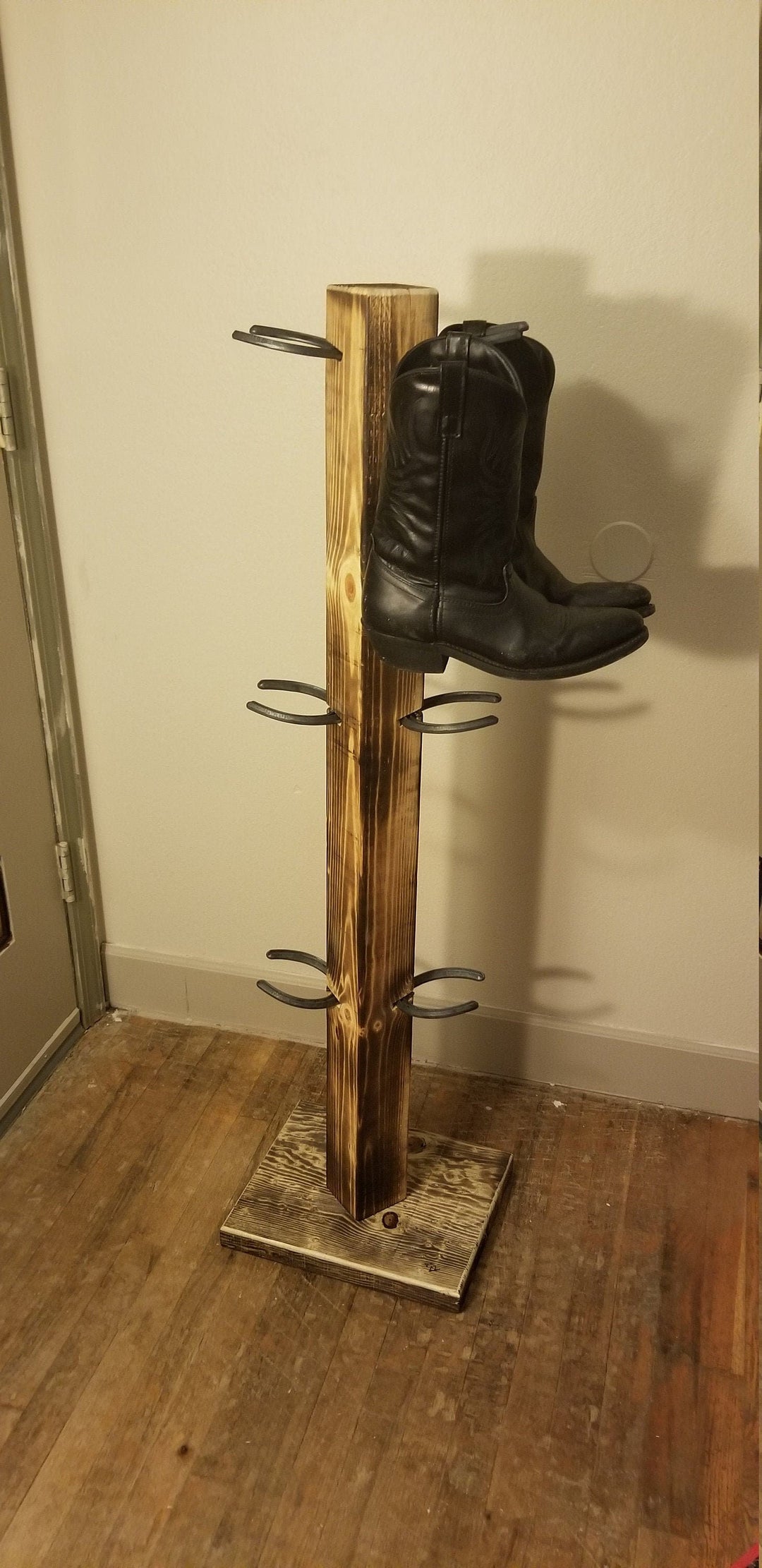 Wooden cowboy boot floor stand with vertical post and 6 side pegs, holding one boot.