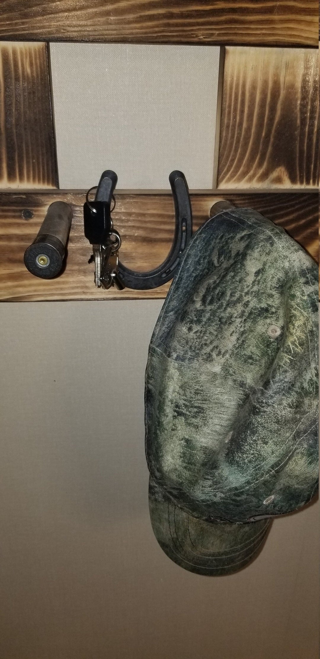 Close-up of wooden wall organizer with central panel, hooks, and dark green hat