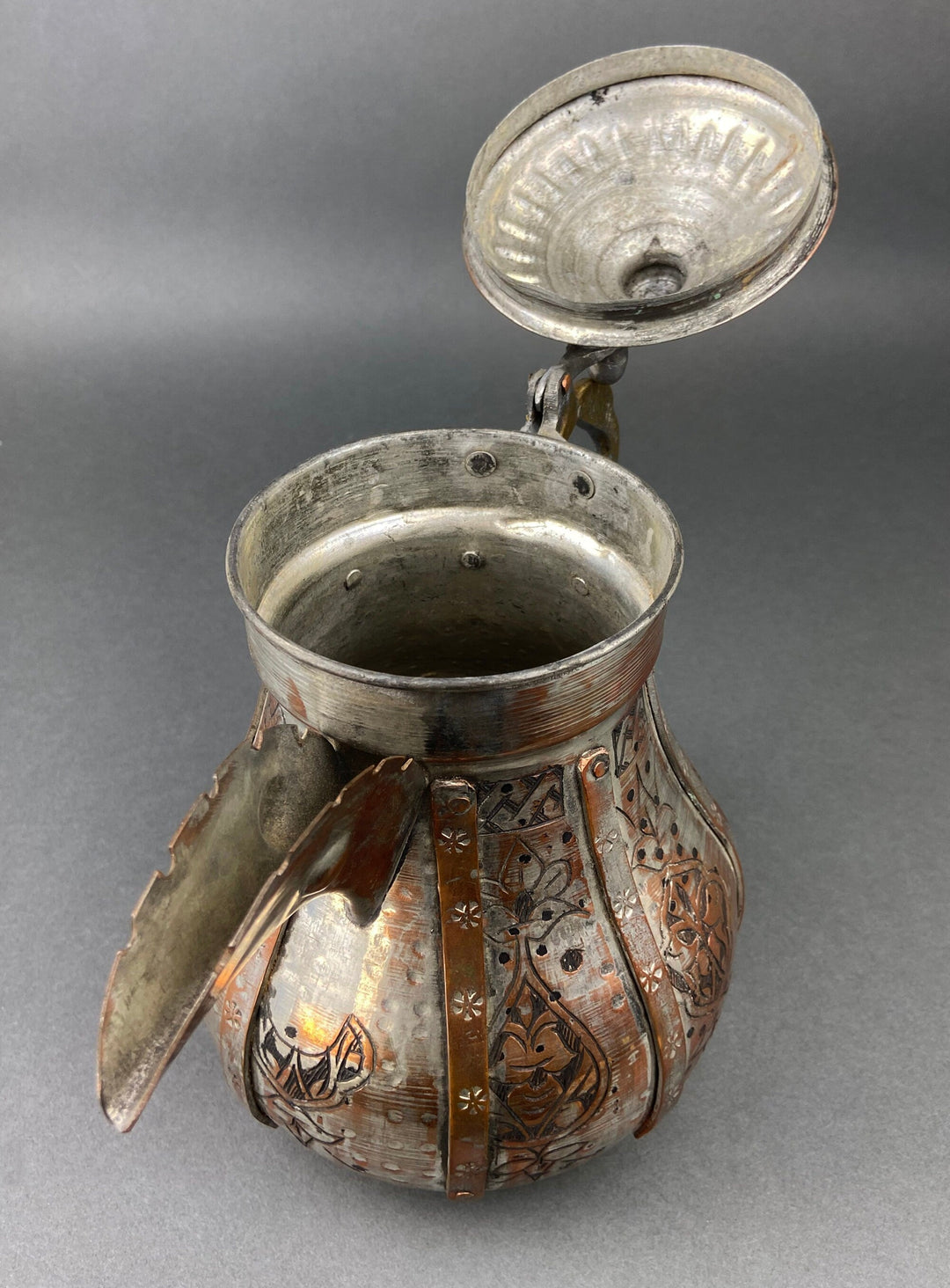Copper coffee pot with lid open, interior dark, ornate embossed front panel and handle