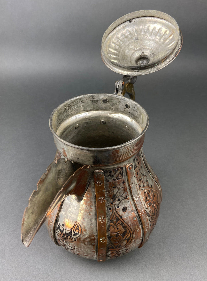 Copper coffee pot with lid open, interior dark, ornate embossed front panel and handle