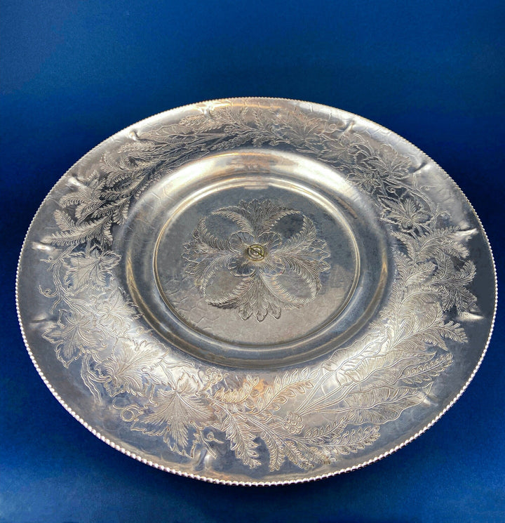 Silver metal serving bowl with raised floral leaf medallion and engraved rim