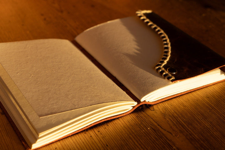 Open brown leather journal with white blanket edge stitching along spine