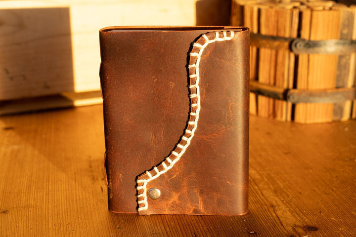 Brown leather journal with white blanket edge stitching and round brass snap button