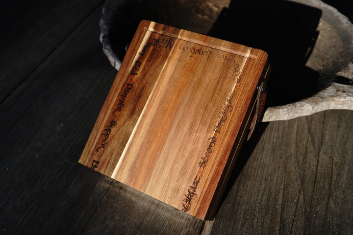 Acacia wood folding cutting board with leather handle, angled view with engraved front panel