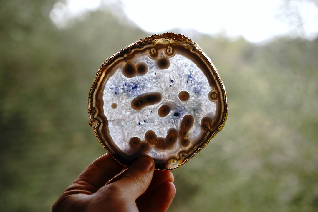 Hand holding a round blue agate coaster back with gold rim and mottled surface