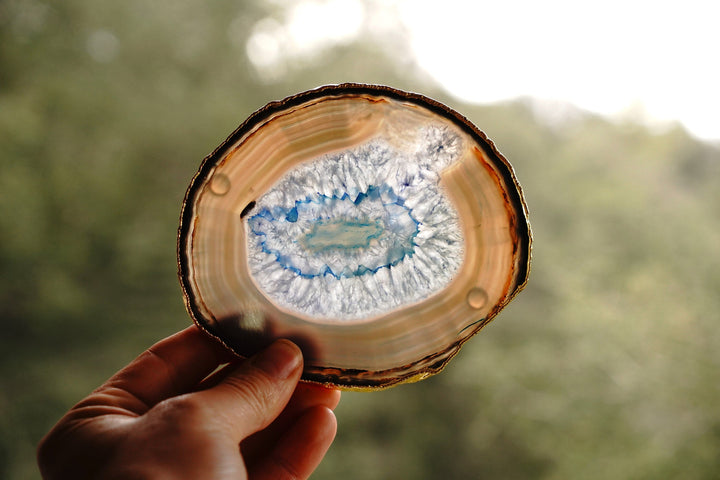 Hand holding a round blue agate coaster with a gold rim and blue center pattern