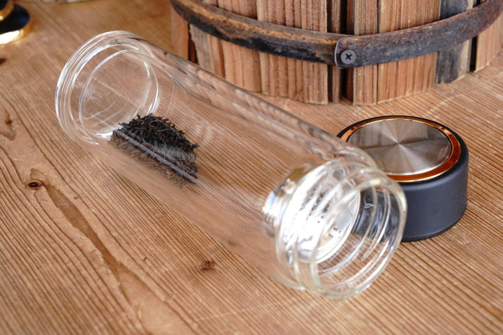 Tea infuser glass tumbler with black lid and visible tea basket mesh inside