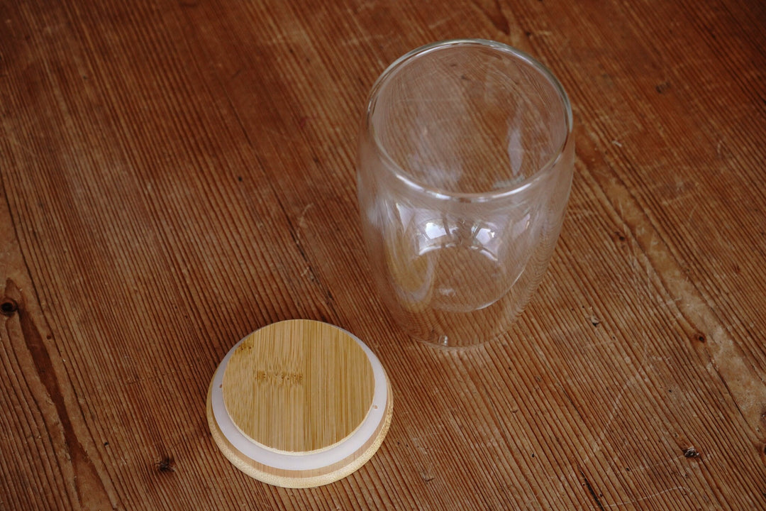 Double-walled glass mug with bamboo lid and rubber seal ring, shown empty on table.