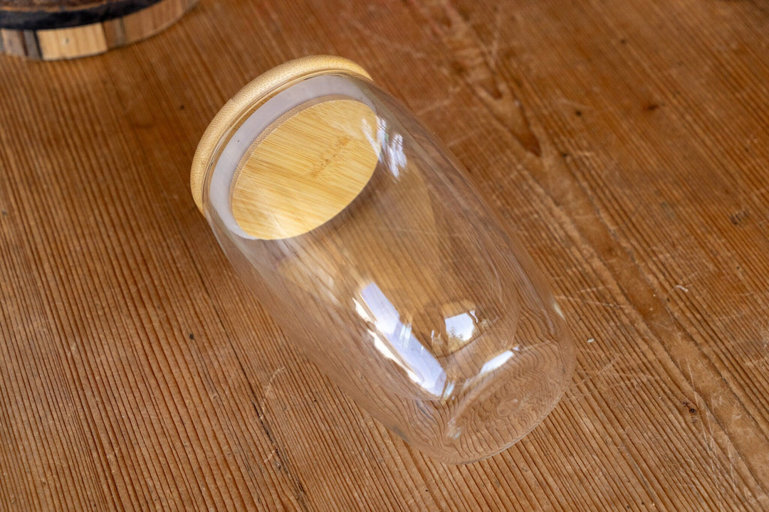 Double-walled glass mug with bamboo lid, clear cup viewed from an angled side.