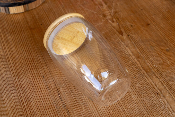 Double-walled glass mug with bamboo lid, clear cup viewed from an angled side.