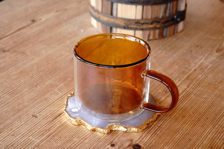 Amber double-walled glass mug with handle, on a round base coaster