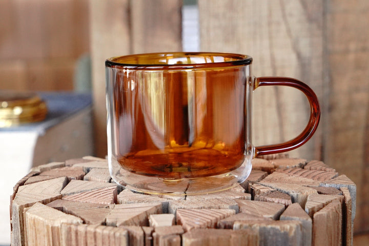 Amber double-walled glass tea/coffee mug with handle on a wooden coaster