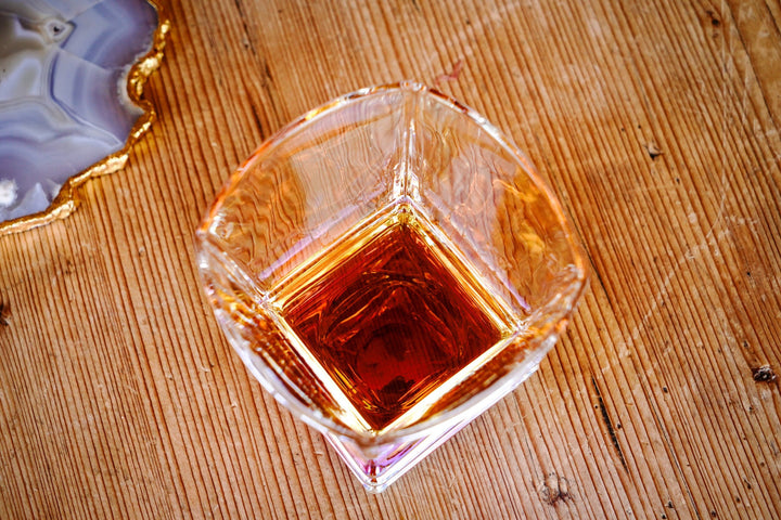 Iridescent whiskey glass bottom view with dark amber liquid and faceted sides