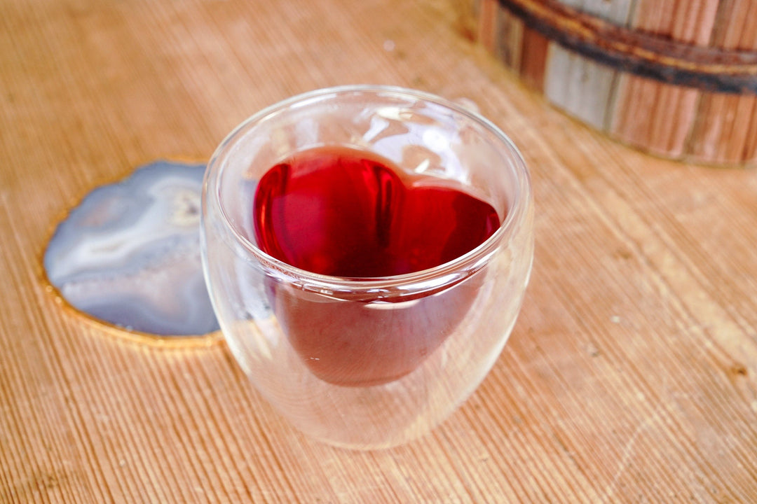 Clear double-walled glass mug filled with red tea, heart-shaped insert