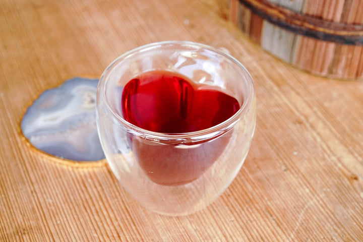 Clear double-walled glass mug filled with red tea, heart-shaped insert