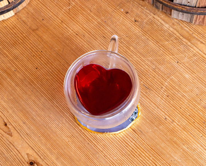 Clear double-walled glass mug with red tea and heart-shaped insert, handle up