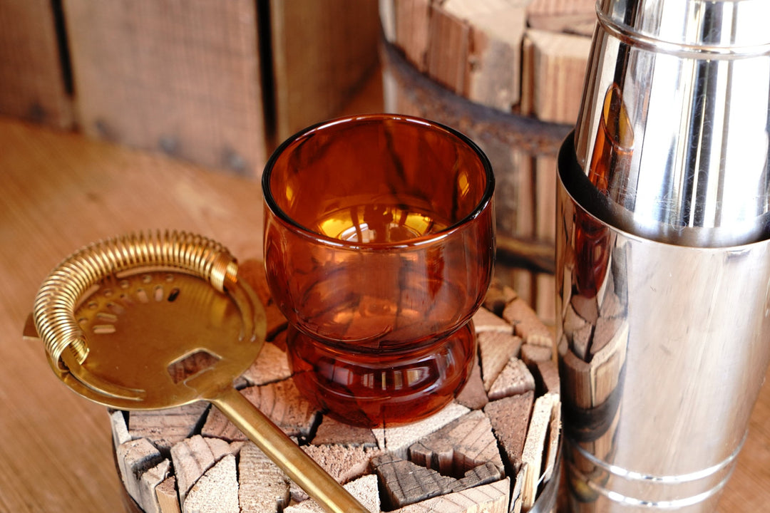 Amber orange bubble juice glass beside a brass-colored tray and metal cylinder
