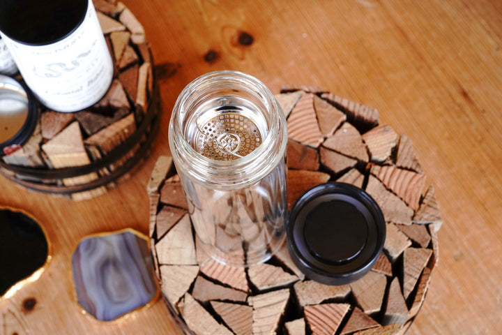 Tea infuser glass tumbler with open top and black base cap beside it