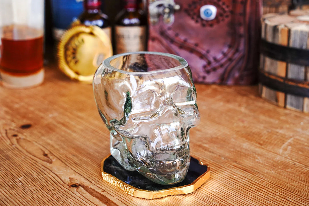 Skull-shaped whiskey glass with detailed face on black coaster